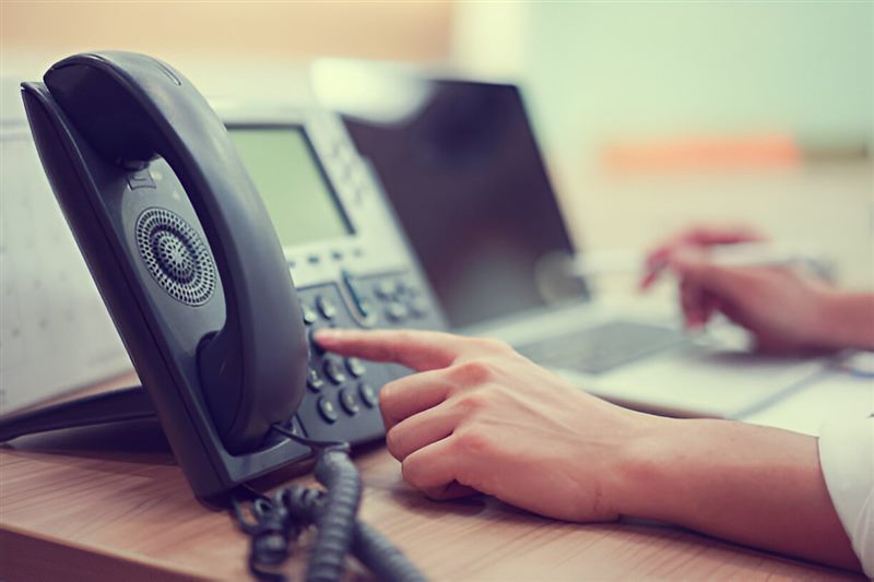 A hand dialling on an office desk phone